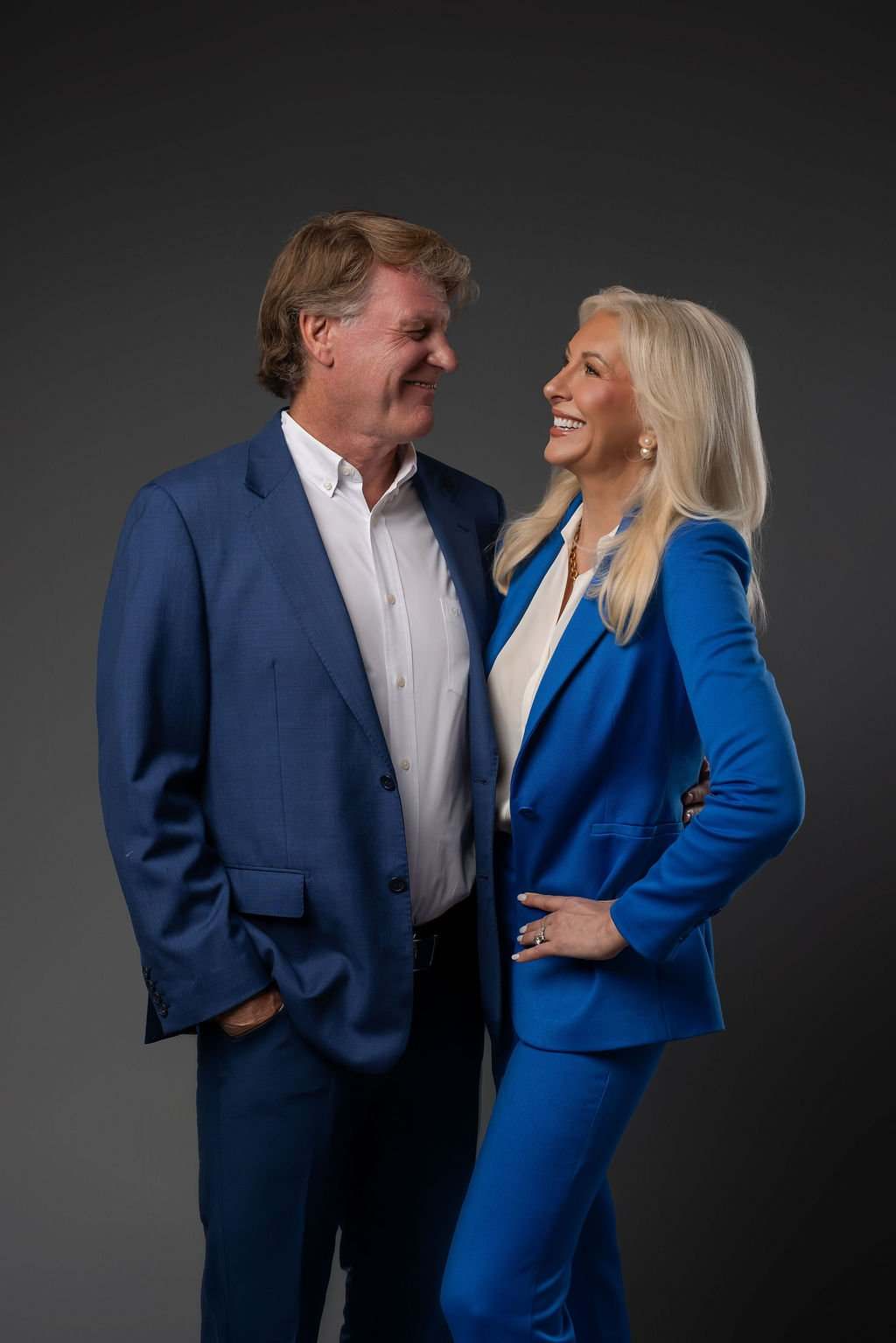 Dr. Paul Keck and Dr. Tracey Skale smiling at each other in blue suits against a dark backdrop