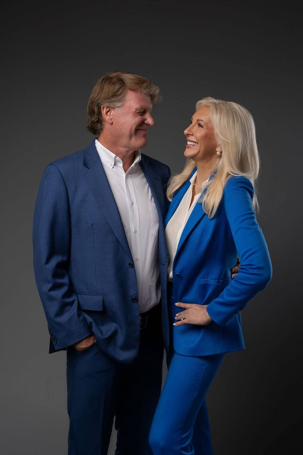 Dr. Paul Keck and Dr. Tracey Skale smiling at each other in blue suits against a dark backdrop